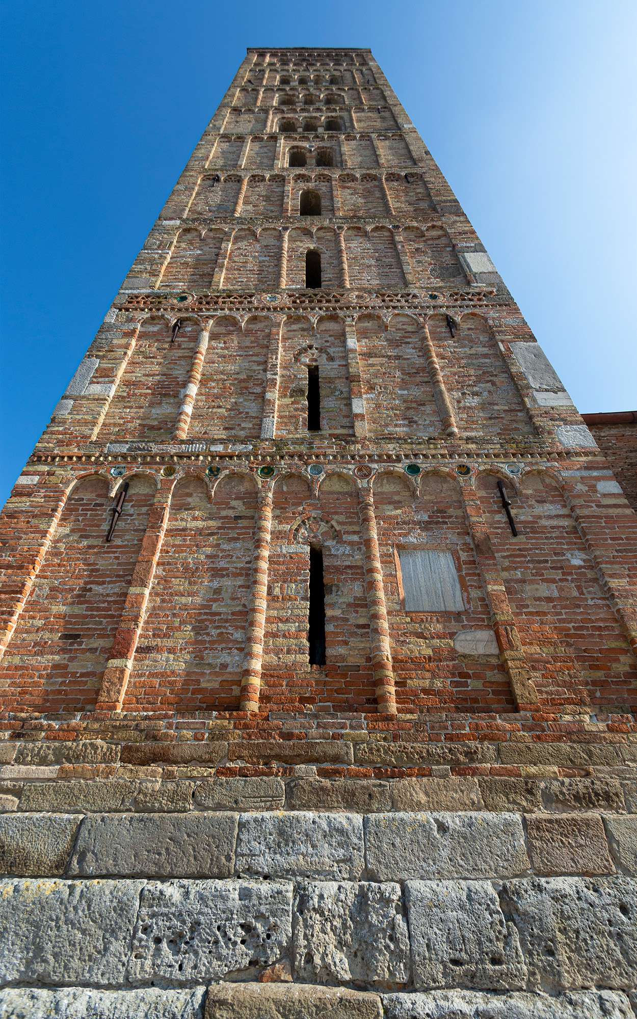 Campanile dell'Abbazia di Pomposa visto dal basso. Il campanile è una struttura di mattoni rossi a vista con decori architettonici.